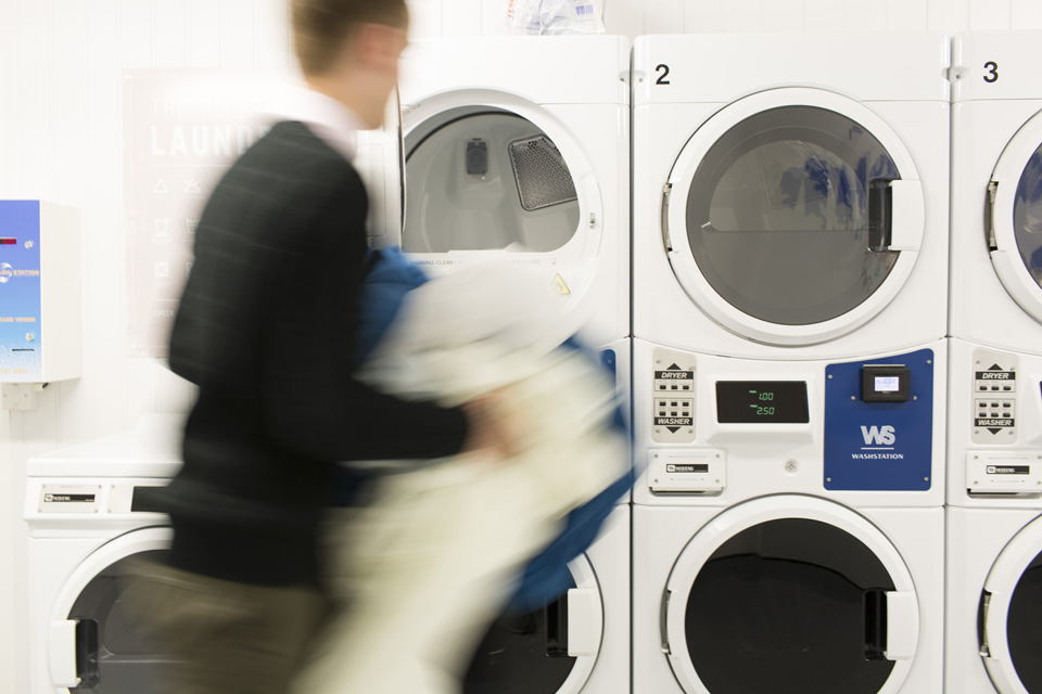 A series of laundry machines stacked together, with a student going to put clothes in an empty one.